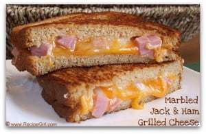 Side view of halved marbled jack and ham grilled cheese stacked on a white plate. 