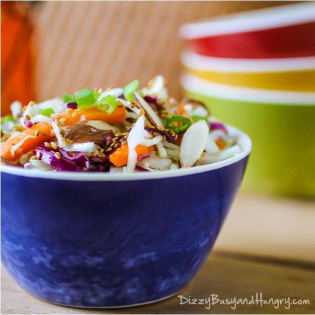 Side view of ramen noodle coleslaw in a blue bowl with more colorful bowls in the background.