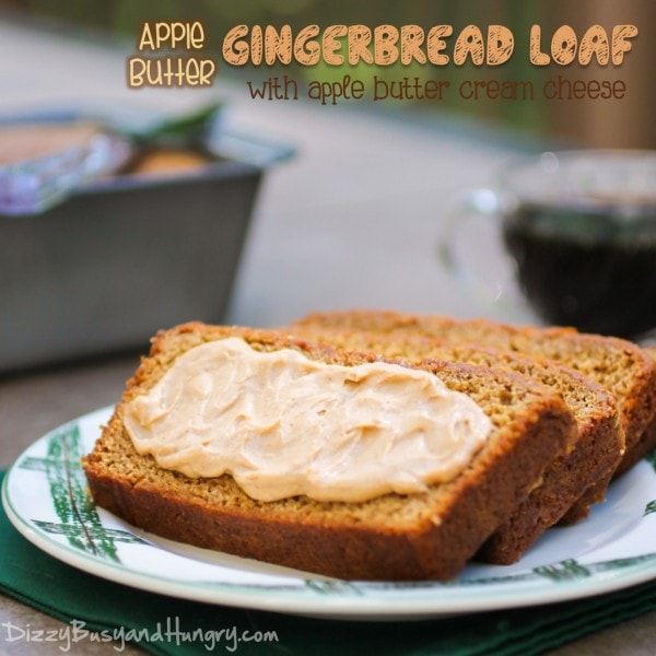 Side view of three slices of apple butter gingerbread loaf with apple butter cream cheese spread on the front stacked on a white plate with a cup of coffee in the background. 