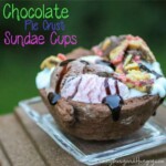 Side view of chocolate pie crust sundae cup drizzled with chocolate syrup on a clear plate on a wooden surface.