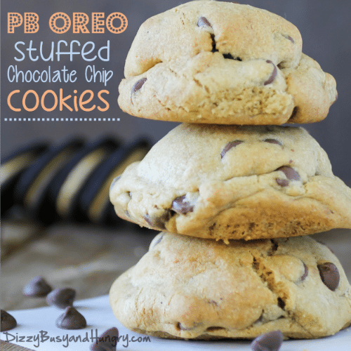 Side view of three PB Oreo chocolate chip cookies stacked on a white paper on a wooden surface with chocolate chips and Oreos in the background. 