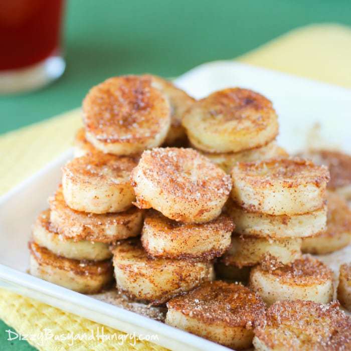 Side view of pan fried cinnamon bananas stacked on a white plate on a yellow and green cloth. 