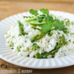 Close up shot of cilantro lime asparagus and rice garnished with cilantro in a white bowl on a wooden table.