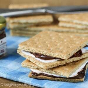 Side shot to two lunchbox S'mores stacked on a blue plaid cloth with more graham crackers in the background.