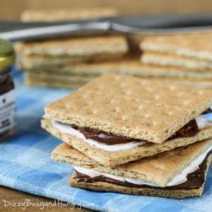 Side shot to two lunchbox S\'mores stacked on a blue plaid cloth with more graham crackers in the background. 