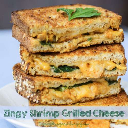 Side view of four stacked halves of zingy shrimp grilled cheese on a white plate. 
