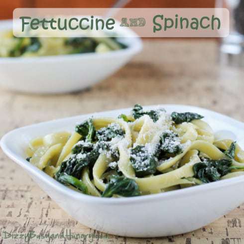 Side view of fettuccine and spinach in a white bowl on a wooden table. 