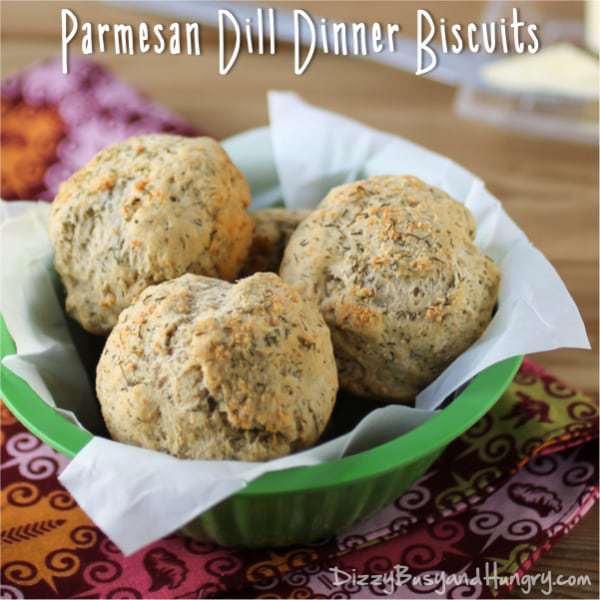 Side view of parmesan dill dinner biscuits in a green bowl lined with white paper on a purple and orange cloth.