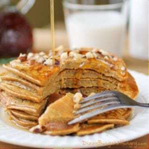 Side shot of pumpkin apple butter pancakes stacked on a white plate with a piece taken out with a fork.