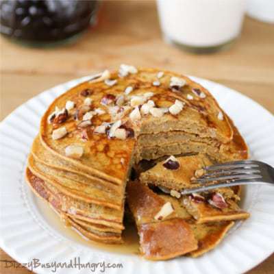 Side shot of pumpkin apple butter pancakes stacked on a white plate with a piece taken out with a fork.