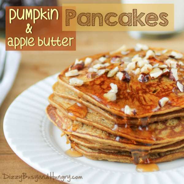 Side shot of pumpkin apple butter pancakes garnished with syrup and nuts on a white plate on a wooden table.