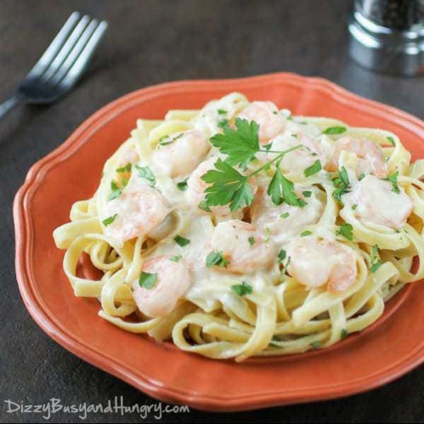 Side view of shrimp fettuccine Alfredo garnished with herbs on a red plate with a fork on the side.