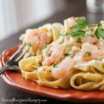 Close up shot of shrimp fettuccine Alfredo garnished with herbs on a red plate with a fork on the side.