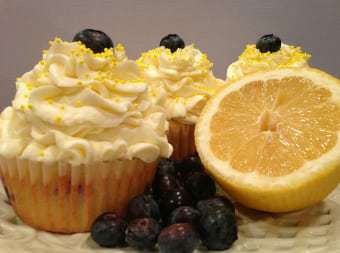 Side view of three mascarpone lemon blueberry cupcakes with a halved lemon and blueberries in the front. 