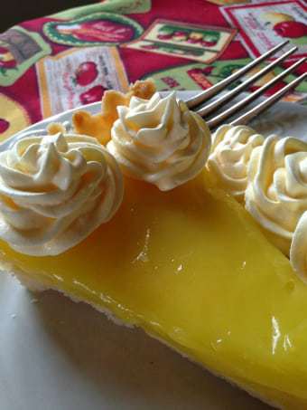 Close up shot of a slice of lemon tart on a white plate with a fork on the side. 