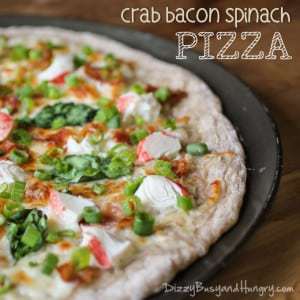 Side view of half bacon crab spinach pizza on a dark pizza tray garnished with scallions.