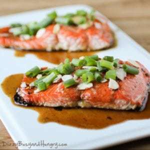 Side shot of two maple glazed salmon pieces garnished with almonds and chives on a white plate.