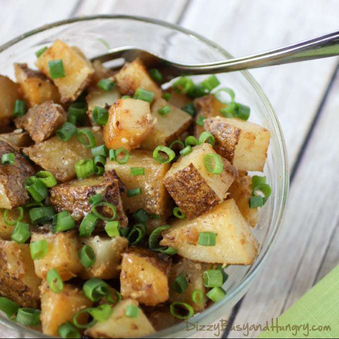 Overhead shot of chipotle and garlic grilled potatoes in a clear bowl with a fork on a green cloth. 