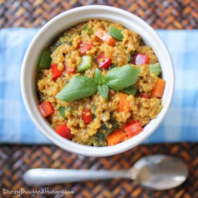 Overhead shot of spicy veggie quinoa curry in a white bowl on a blue plaid cloth with a spoon on the side.