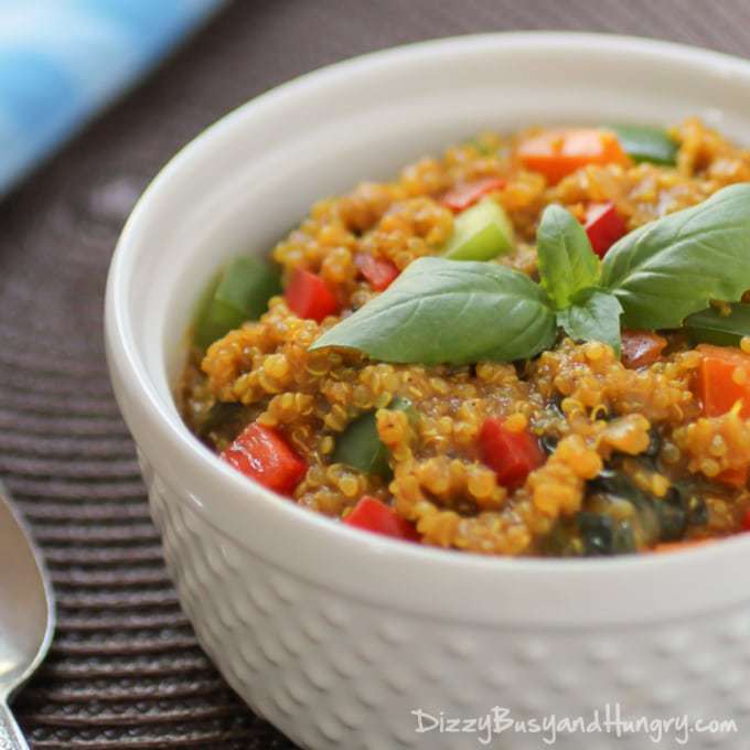 Close up shot of spicy veggie quinoa curry garnished with herbs in a white bowl with a spoon on the side. 