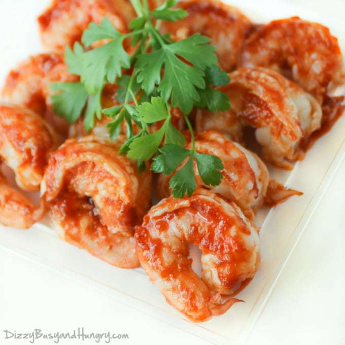 Overhead shot of sweet and spicy grilled shrimp garnished with herbs on a white plate.