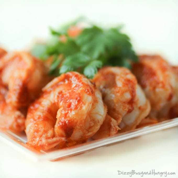 Close up shot of sweet and spicy grilled shrimp garnished with herbs on a white plate.