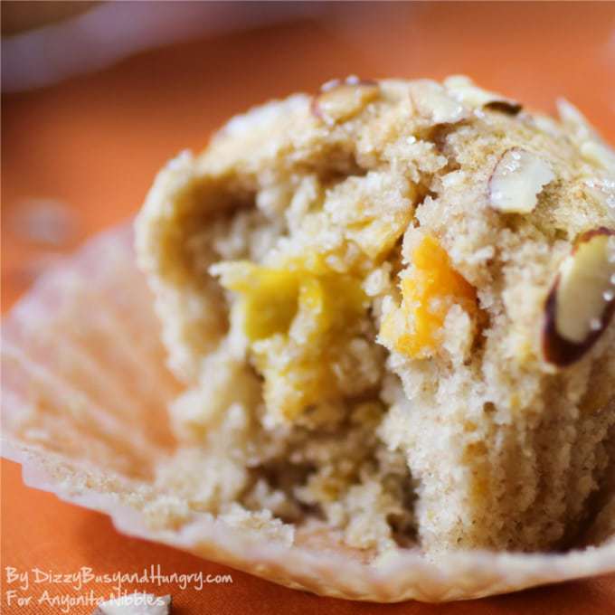 Close up shot of a mango muffin in unwrapped liner with an orange background. 