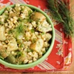 Overhead shot of potato and grilled corn salad in a green bowl on a red cloth.