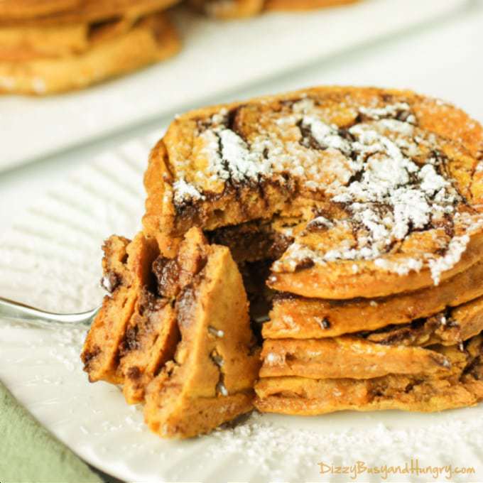 Side view of a fork taking a slice of pumpkin chocolate swirl pancakes stacked on a white plate. 