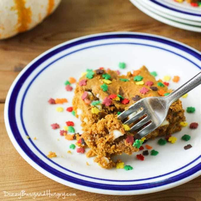 Side view of a fork taking a piece of white chocolate chip pumpkin cake on a white and blue striped plate. 