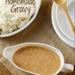 Overhead shot of homemade gravy in a white gravy boat with a bowl of mashed potatoes and a wooden spoon on the side. 