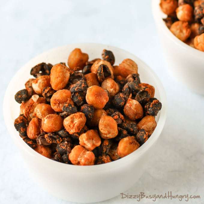 Close up shot of two white bowls of chickpea and black bean snack mix with spices in the background. 
