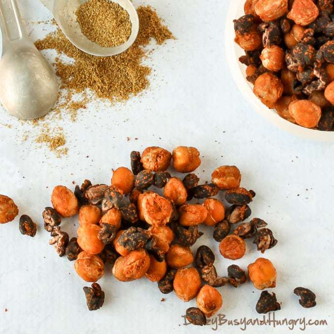 Close upshot of chickpea and black bean snack mix sprinkled on a white surface with spices in the background.