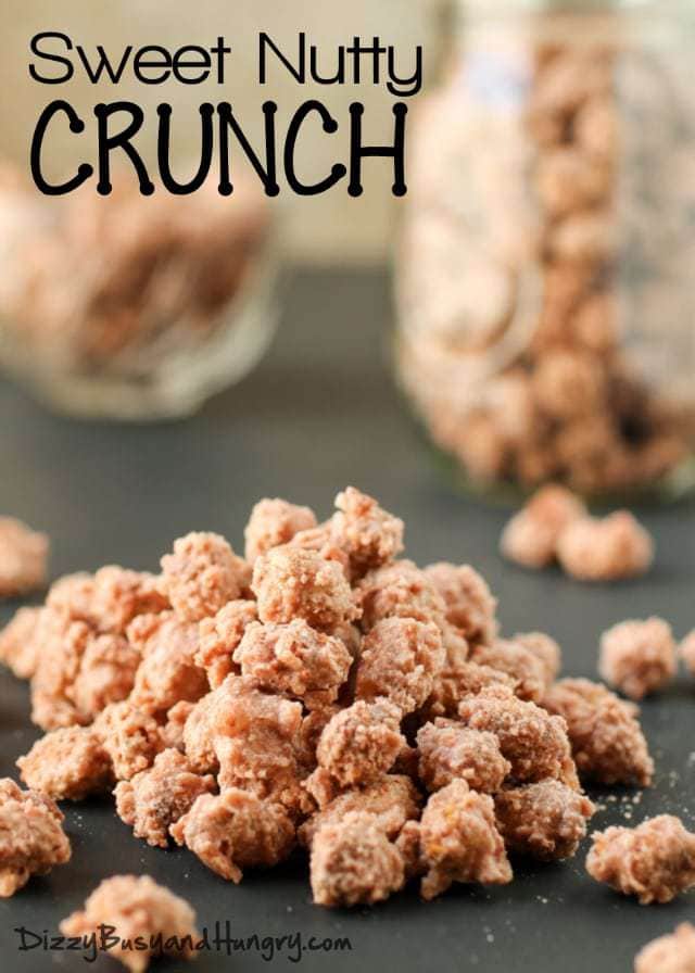 Close up shot of sweet nutty crunch on a black surface with jars of it in the background. 