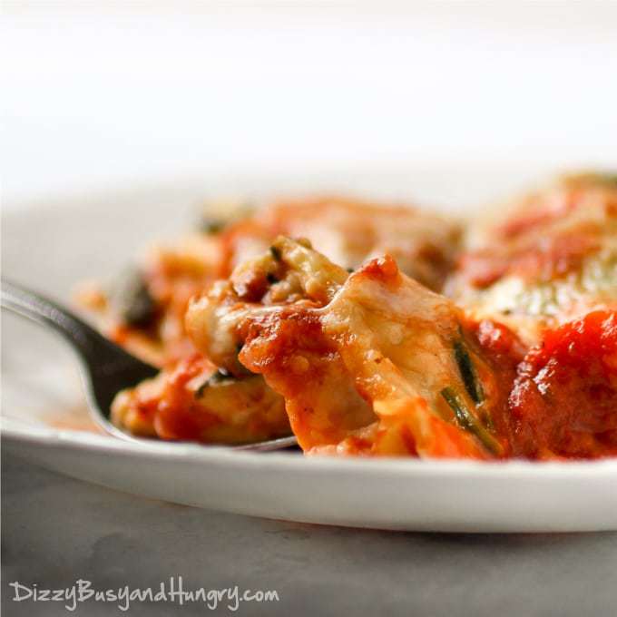 Close up shot of ravioli spinach bake on a white bowl with a fork.