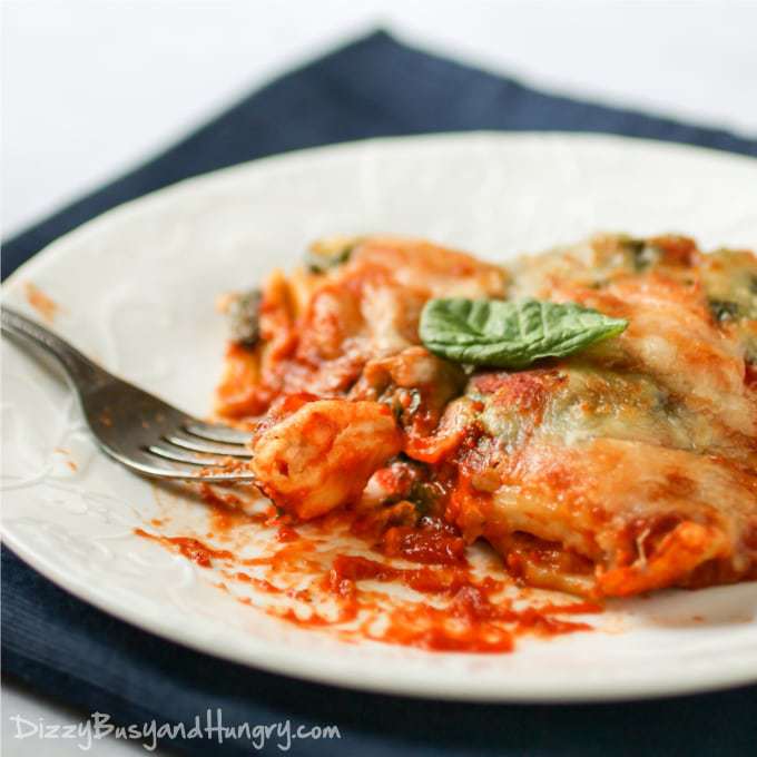 Side view of ravioli spinach bake on a white bowl with a fork on a blue cloth. 