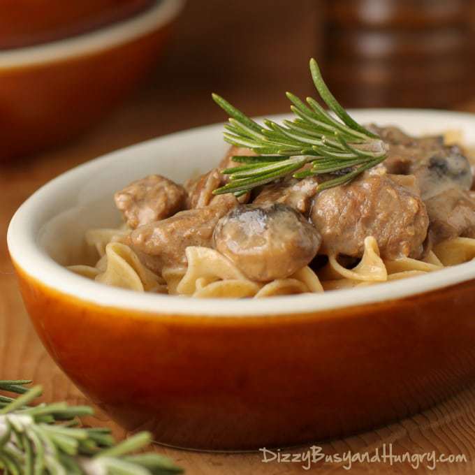 Side shot of crockpot beef stroganoff in an orange oval bowl on a wooden surface. 