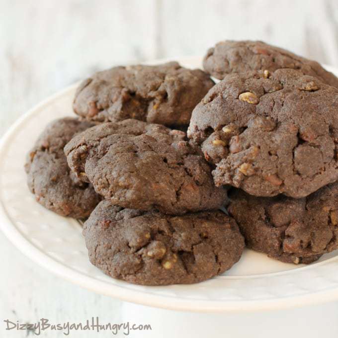 Close up shot of stacked double chocolate crunch cookies on a white plate on a wooden surface. 