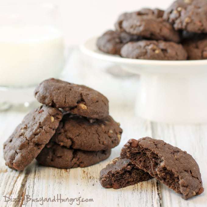 Close up shot of stacked double chocolate crunch cookies on a white plate on a wooden surface. 