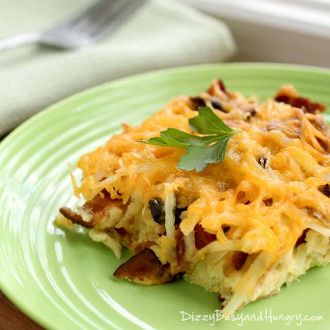 Close up shot of bacon breakfast casserole garnished with herbs on a green plate with a white cloth and a fork on the side.