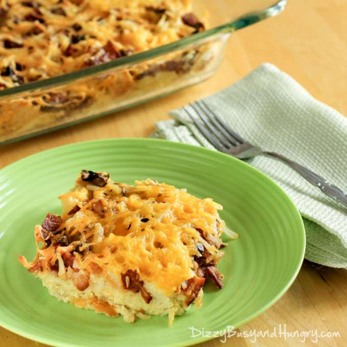 Side view of bacon breakfast casserole on a green plate with a fork on the side with the pan in the background. 