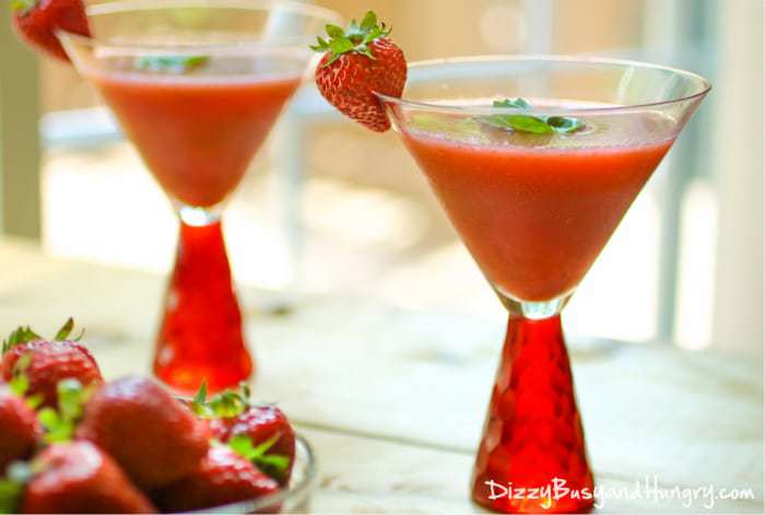 Side view of frozen strawberry basil margaritas garnished with basil and strawberries in red margarita glasses. 