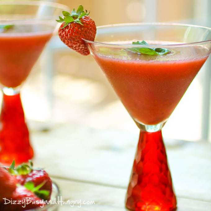 Side view of frozen strawberry basil margaritas garnished with basil and strawberries in red margarita glasses. 
