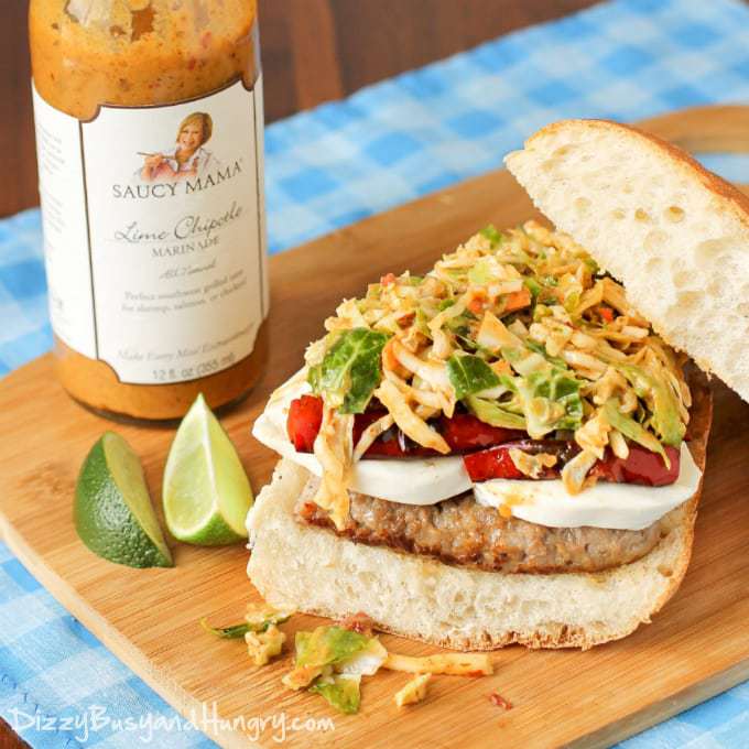 Side shot of sausage mozzarella sandwich on a wooden cutting board with a bottle of chipotle marinade in the background. 