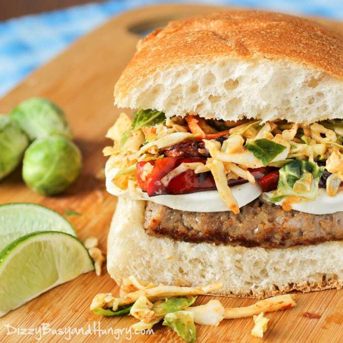 Side shot of sausage mozzarella sandwich with chipotle slaw on a wooden cutting board with sliced lime in the background. 