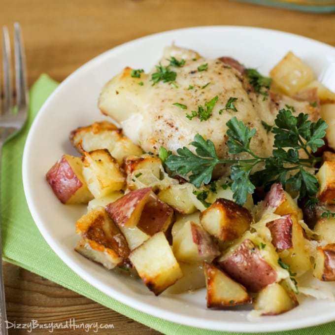 Close up shot of chicken potato bake on a white plate with a fork on the side on a green cloth. 