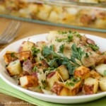 Close up shot of chicken potato bake on a wooden plate with a fork on the side with more in a pan in the background.