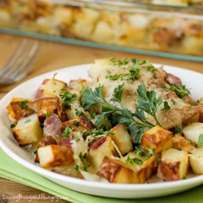 Close up shot of chicken potato bake on a wooden plate with a fork on the side with more in a pan in the background. 