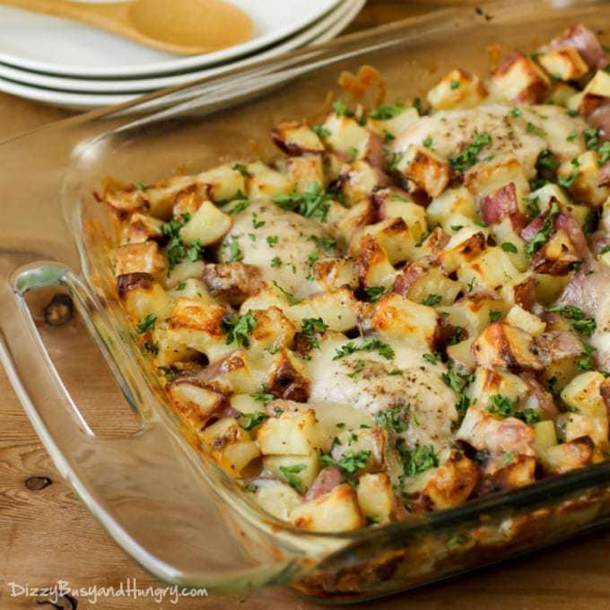 Side view of chicken potato bake in baking pan on a wooden table with white plates and a spoon in the background.