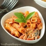 Close up shot of slow cooker baked ziti with mushrooms and spinach garnished with herbs in a white bowl with forks.